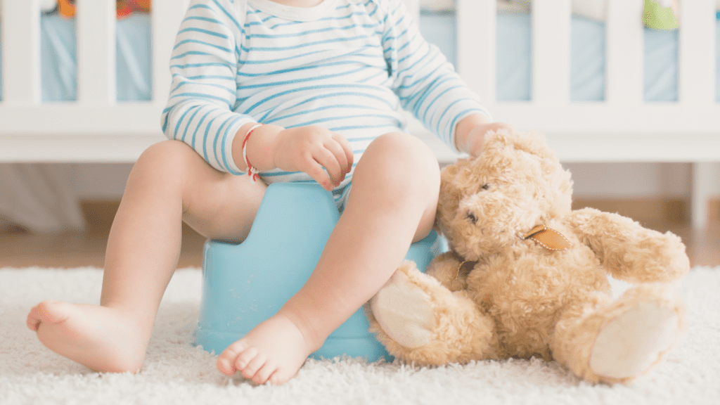 Kind sitzt auf dem Töpfchen und hat einen Teddybär in der Hand